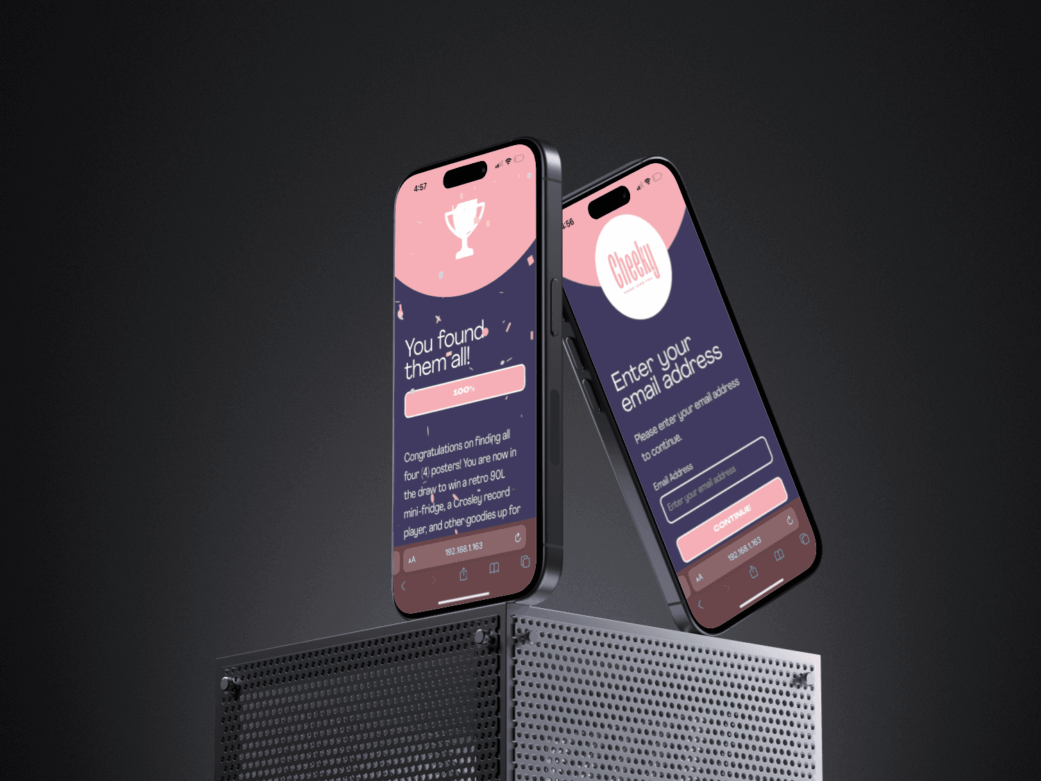 Two smartphones standing on a metal grid, showing a congratulatory message for finding all items in a scavenger hunt on one screen, and an email entry page on the other.